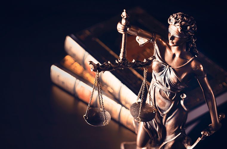 A Lady Justice statue holding scales stands beside stacked law books.
