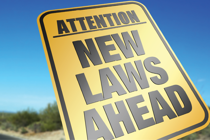 Yellow roadside sign reading ATTENTION NEW LAWS AHEAD beneath a clear blue sky.