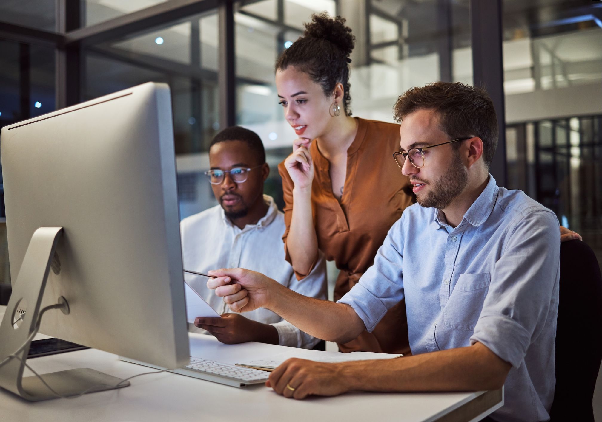 Three coworkers review a desktop monitor, with one pointing toward the screen.