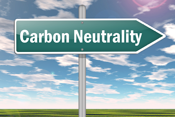 A green arrow sign reading Carbon Neutrality points right beneath a blue sky.