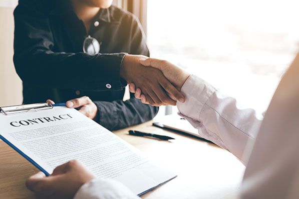 Two people shake hands over a clipboard headed CONTRACT.