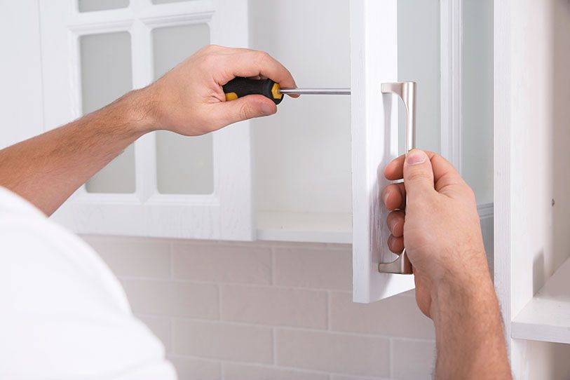 Close-up of hands using a screwdriver to attach a handle to a white cabinet door.
