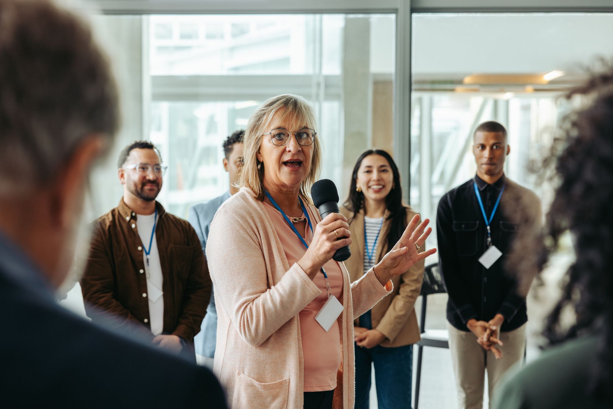 A woman speaks into a handheld microphone to a group of colleagues in an office.