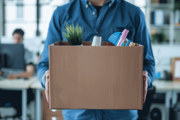 A person carries a cardboard box of office belongings, including a plant and stationery.