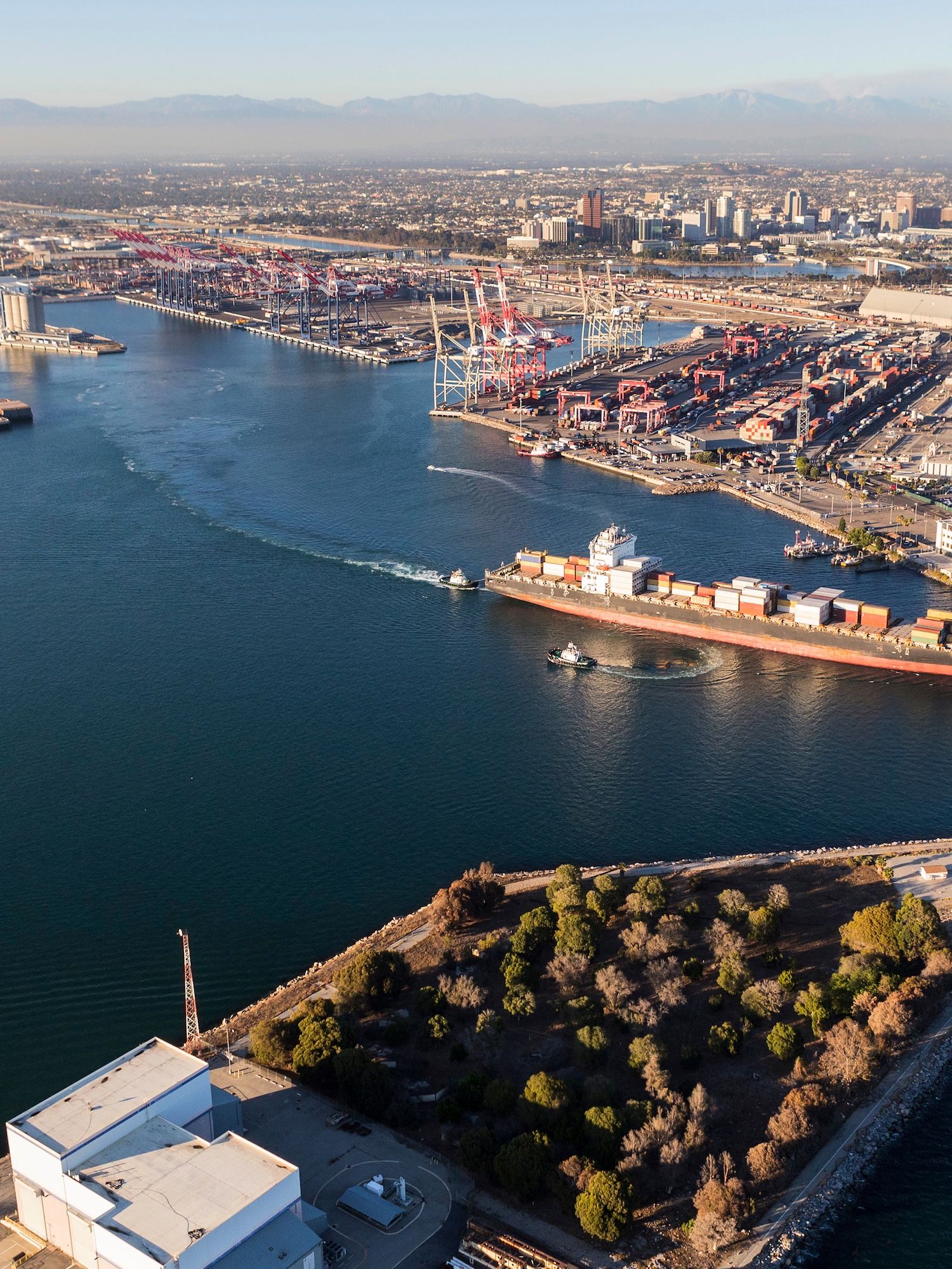 Aerial view of a busy shipping port with container terminals, ships and blue water.