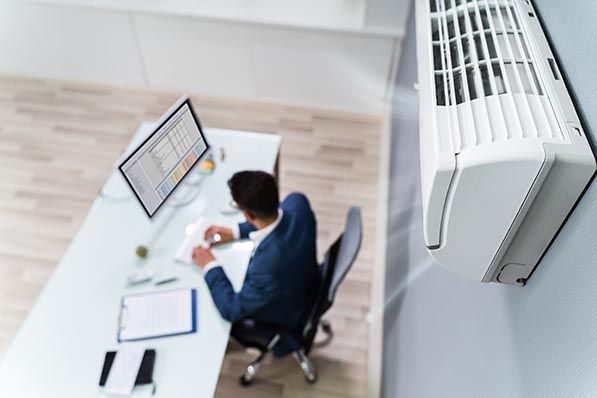 Overhead view of an office worker at a desk beneath a wall-mounted air conditioner.