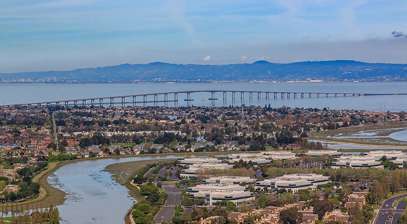 Aerial view of a bayfront city, waterways and a long bridge across the bay.