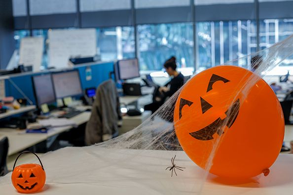 Orange jack-o'-lantern decorations and artificial cobwebs adorn an office desk.