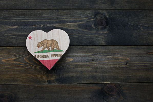 A small wooden heart painted with the California Republic flag on a dark plank background.