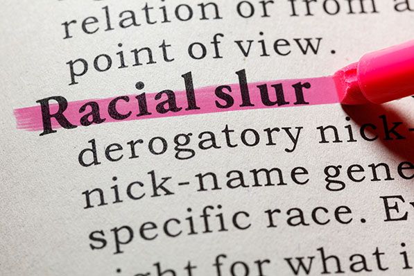 The words Racial slur highlighted in pink in a dictionary beside a pink marker.