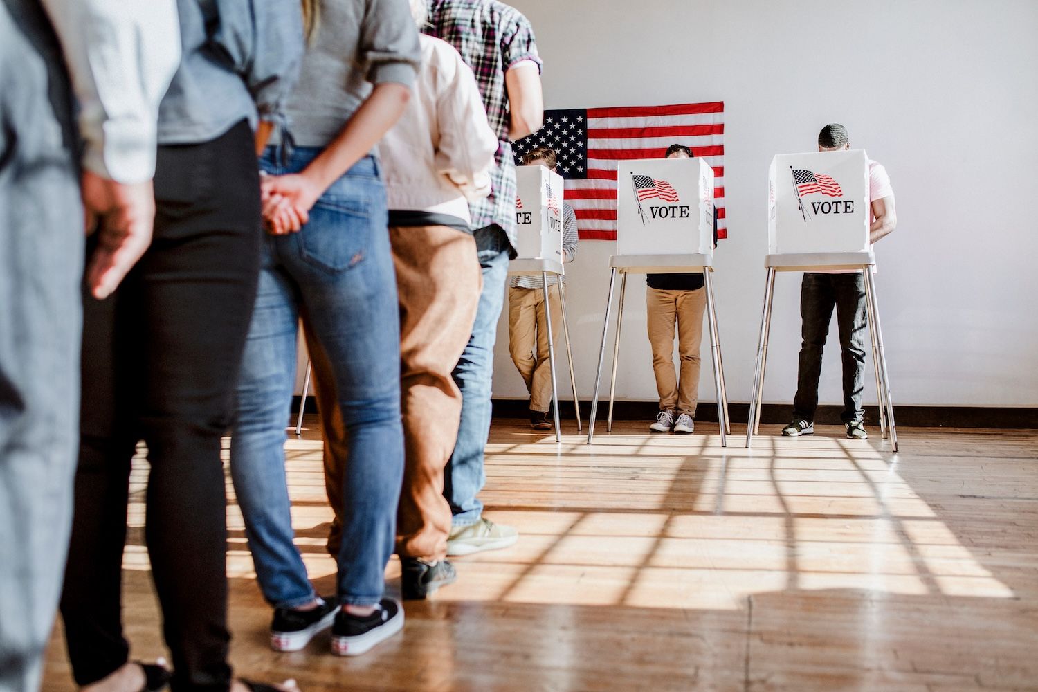 People queue at voting booths beneath a United States flag.
