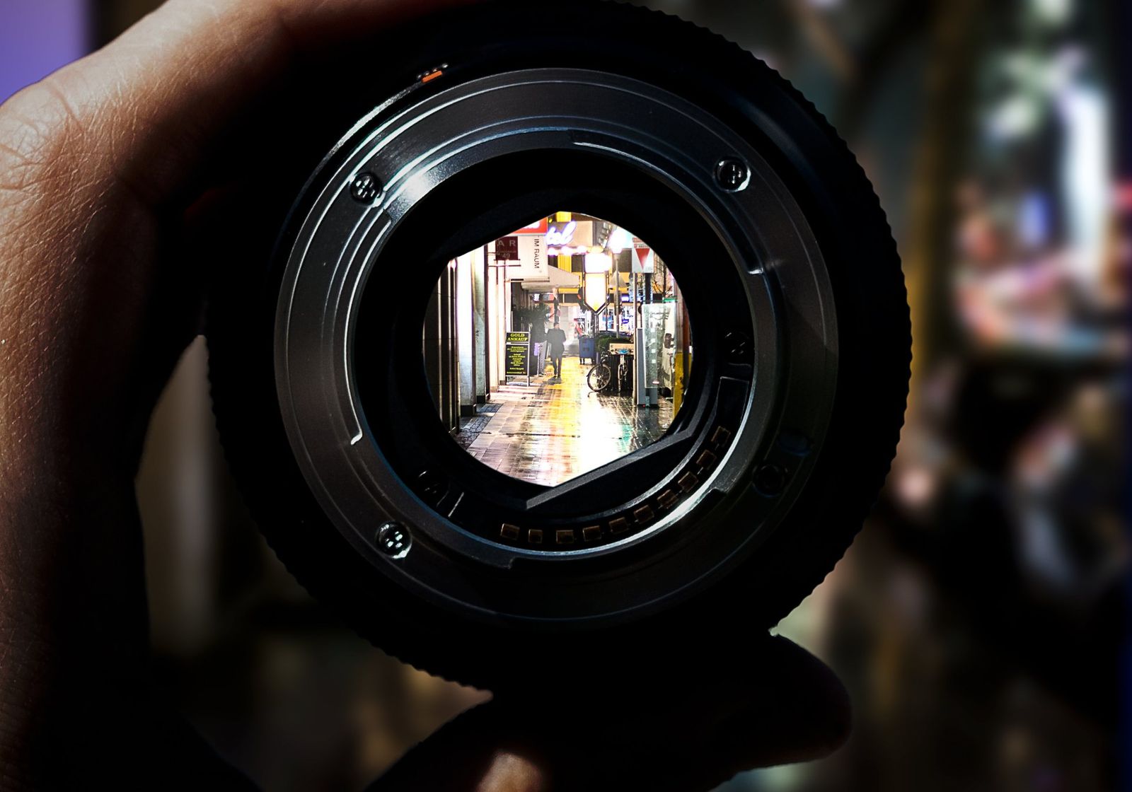 A hand holding a camera lens up to a street, the view sharp inside the glass