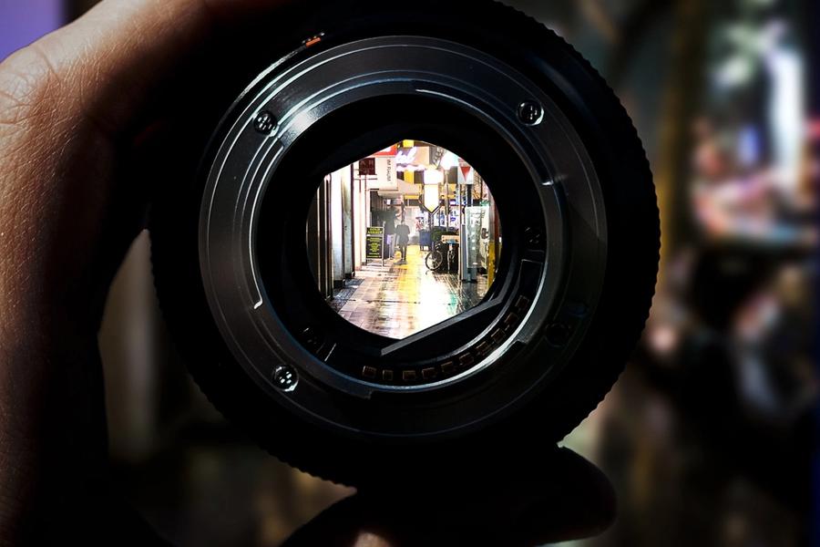 A hand holding a camera lens up to a street, the view sharp inside the glass