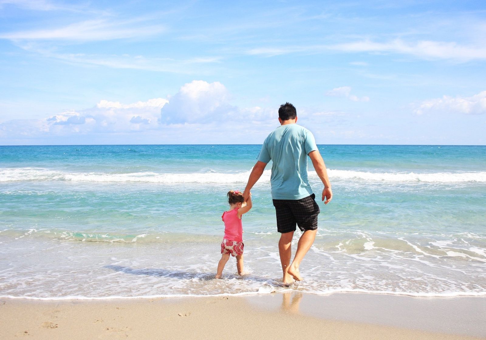 A father and his young daughter walking hand in hand into the surf
