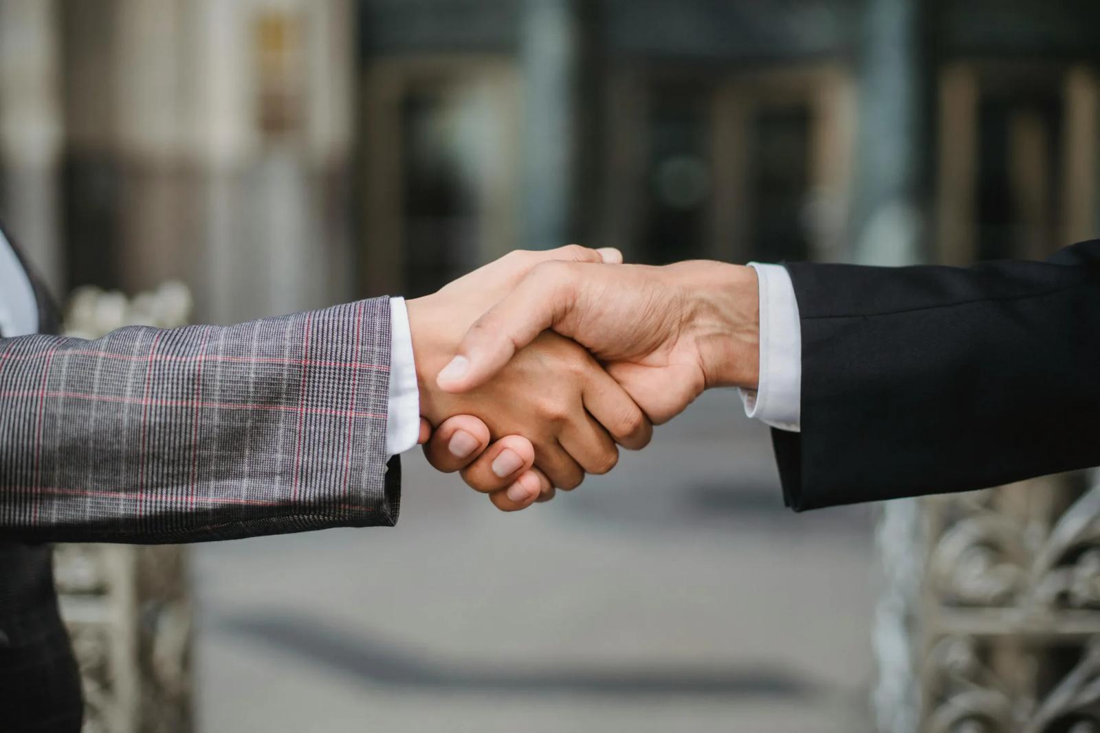 Two people in suits shaking hands outdoors