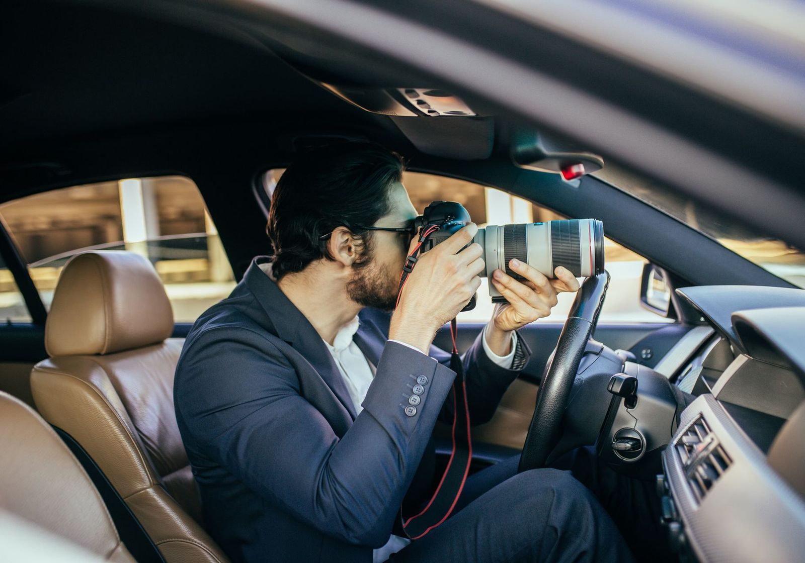 An investigator in a suit photographing through a car window with a long telephoto lens