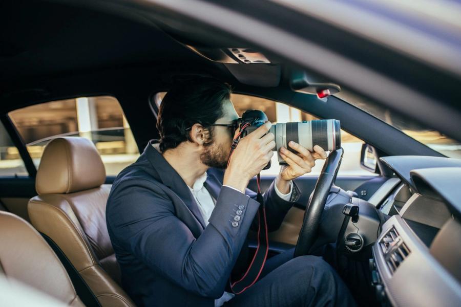 An investigator in a suit photographing through a car window with a long telephoto lens