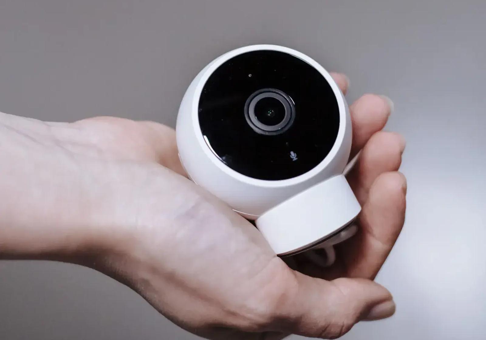 A hand holding a small white dome camera, about to place it