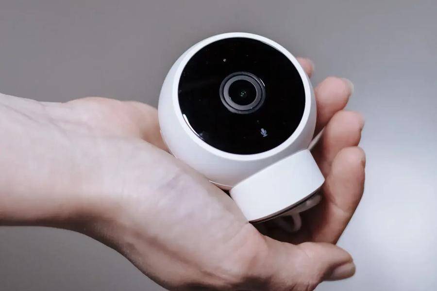 A hand holding a small white dome camera, about to place it