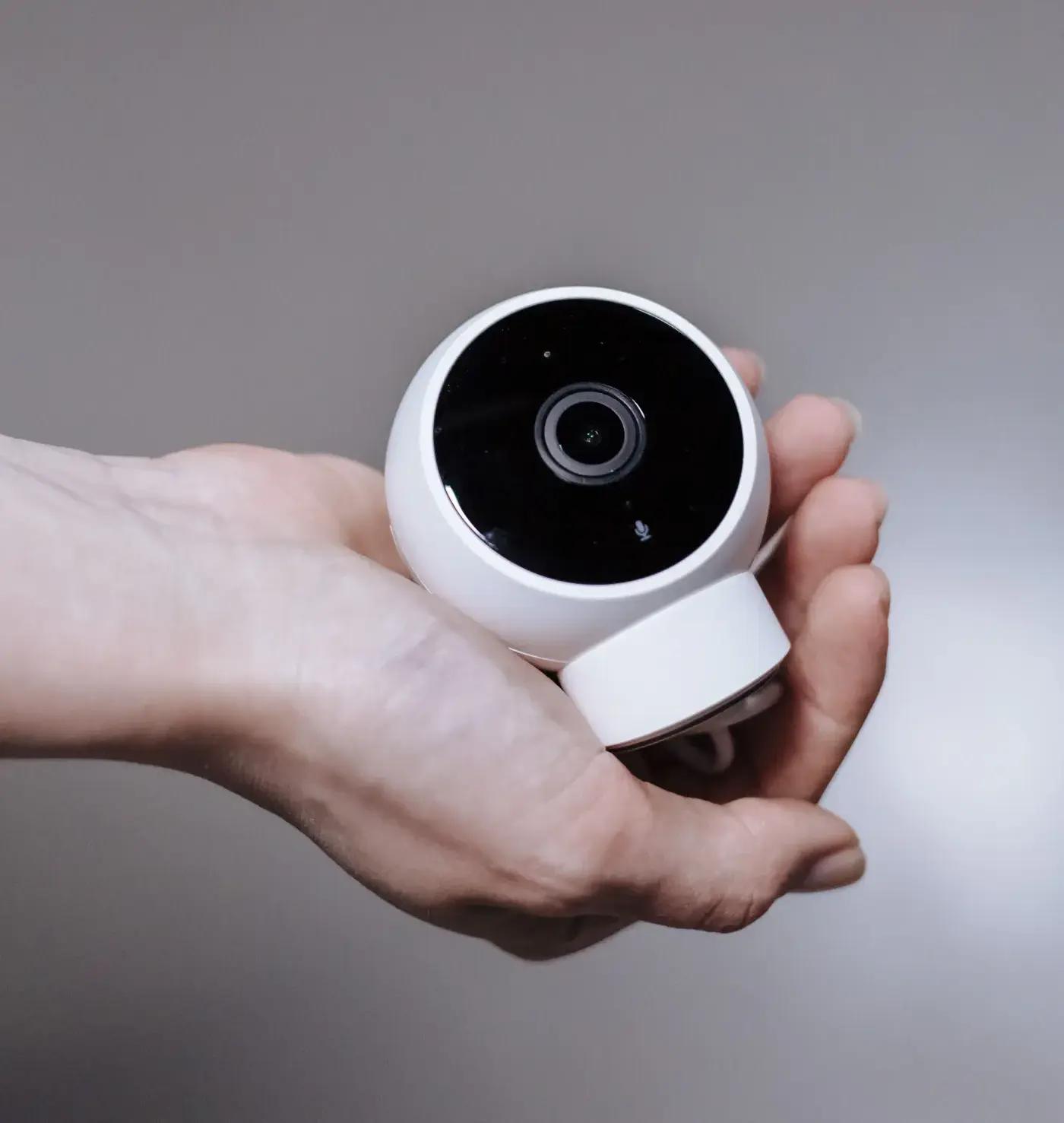 A hand holding a small white indoor security camera