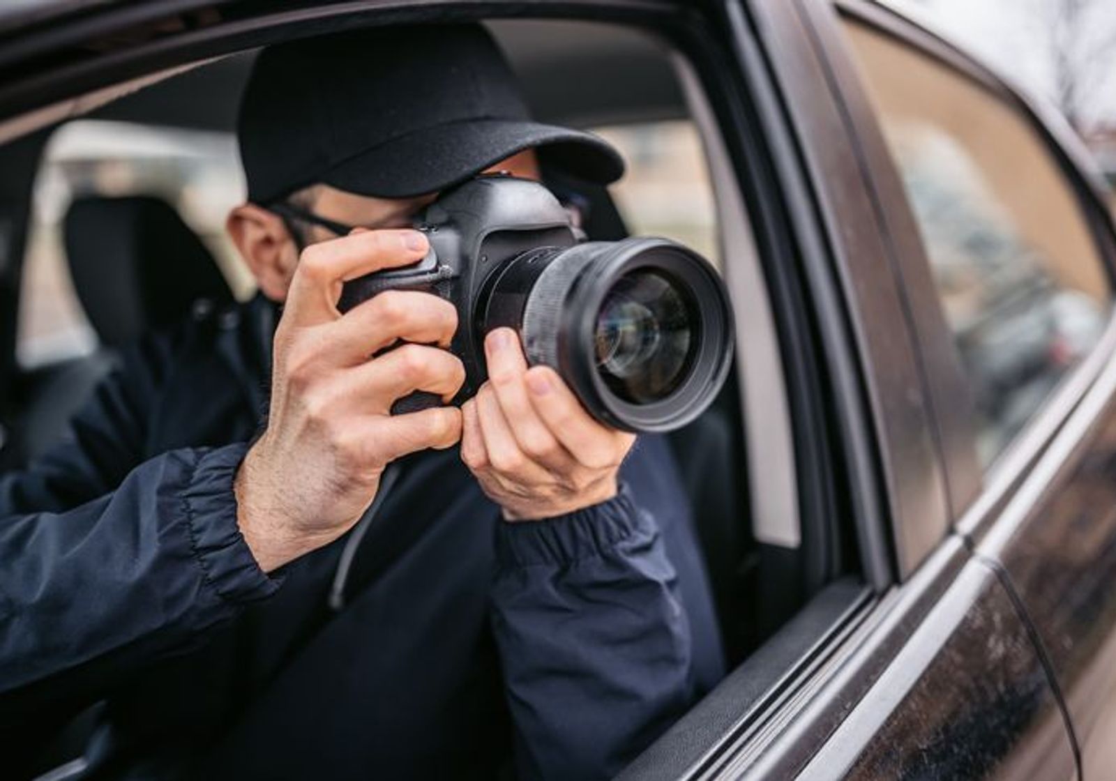 A man in a cap aiming a DSLR out of a car window