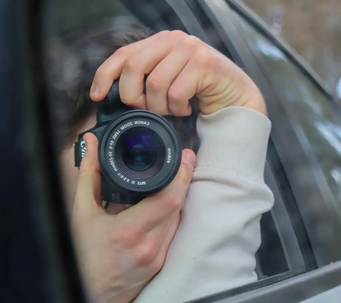 A car's side mirror reflecting someone photographing from the window of another car