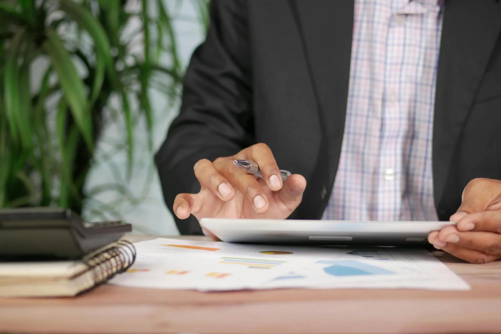 A person in a suit reviewing a tablet over printed charts