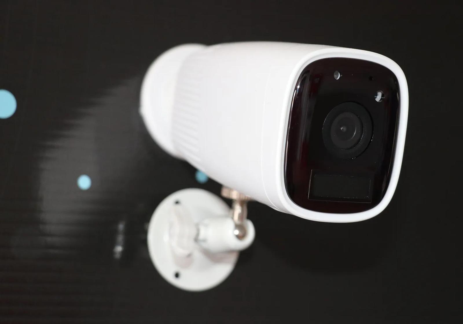 A white bullet security camera on a wall bracket, lit against a dark background