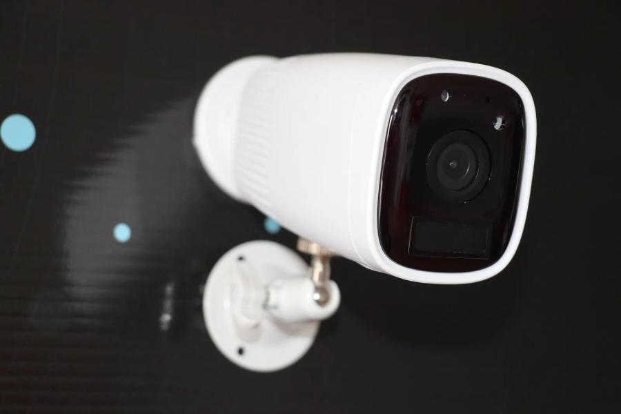 A white bullet security camera on a wall bracket, lit against a dark background