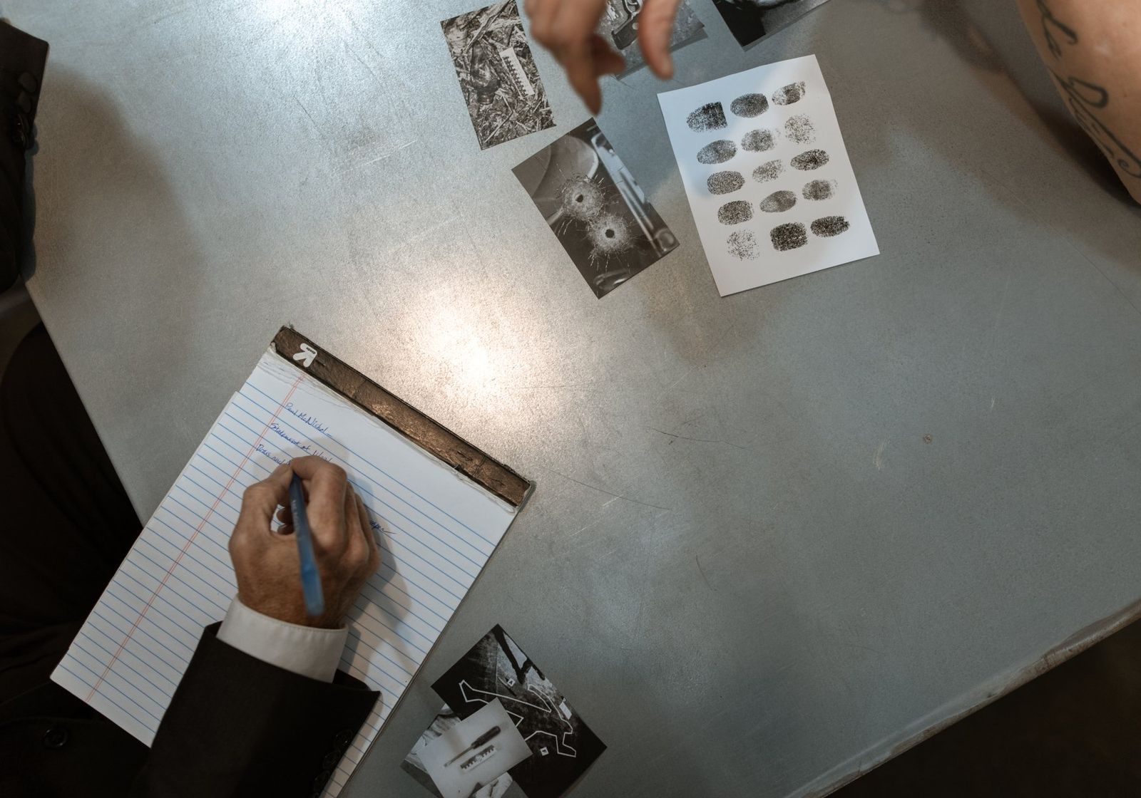 An investigator's desk from above: case photographs, a fingerprint card and a legal pad
