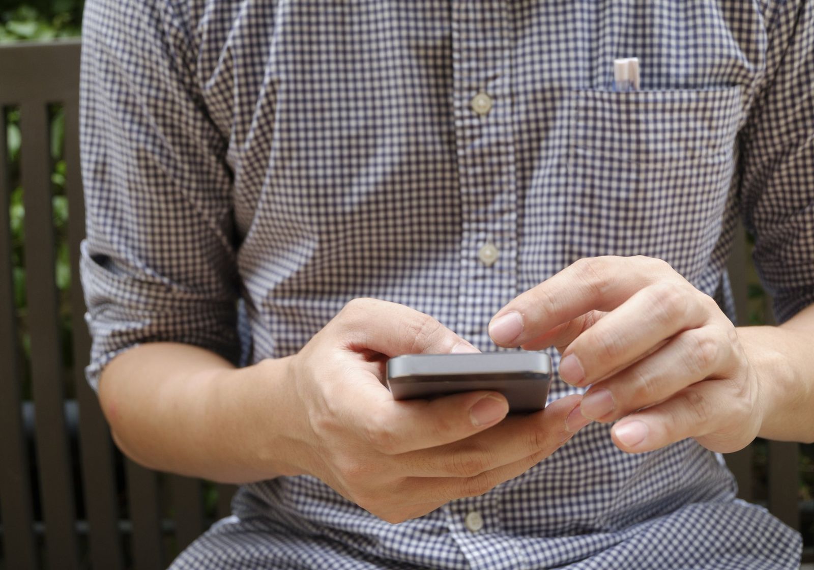 A man in a checked shirt using a smartphone with both hands