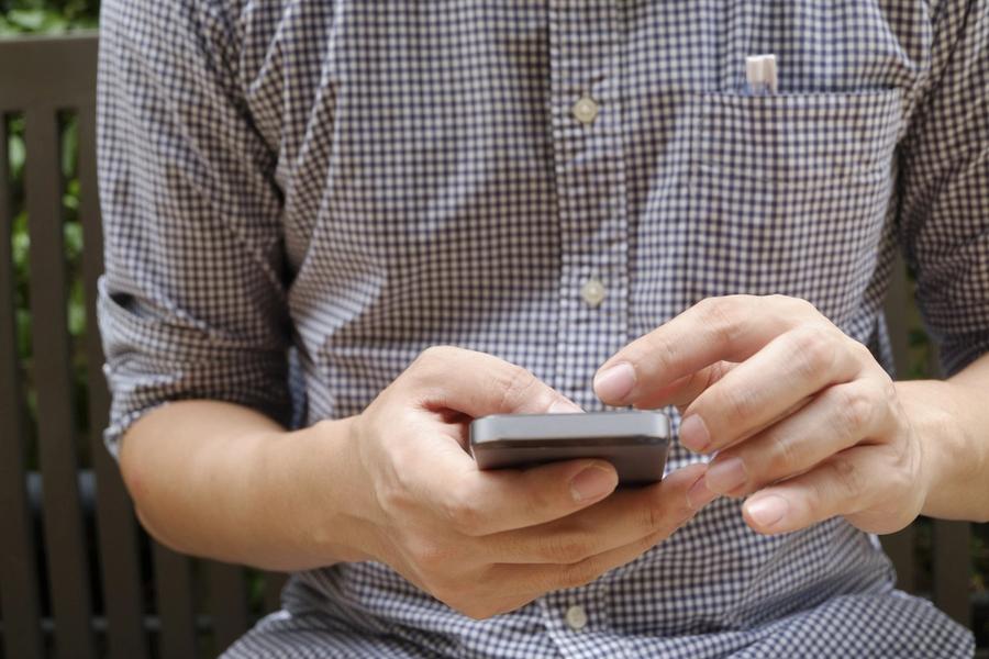 A man in a checked shirt using a smartphone with both hands