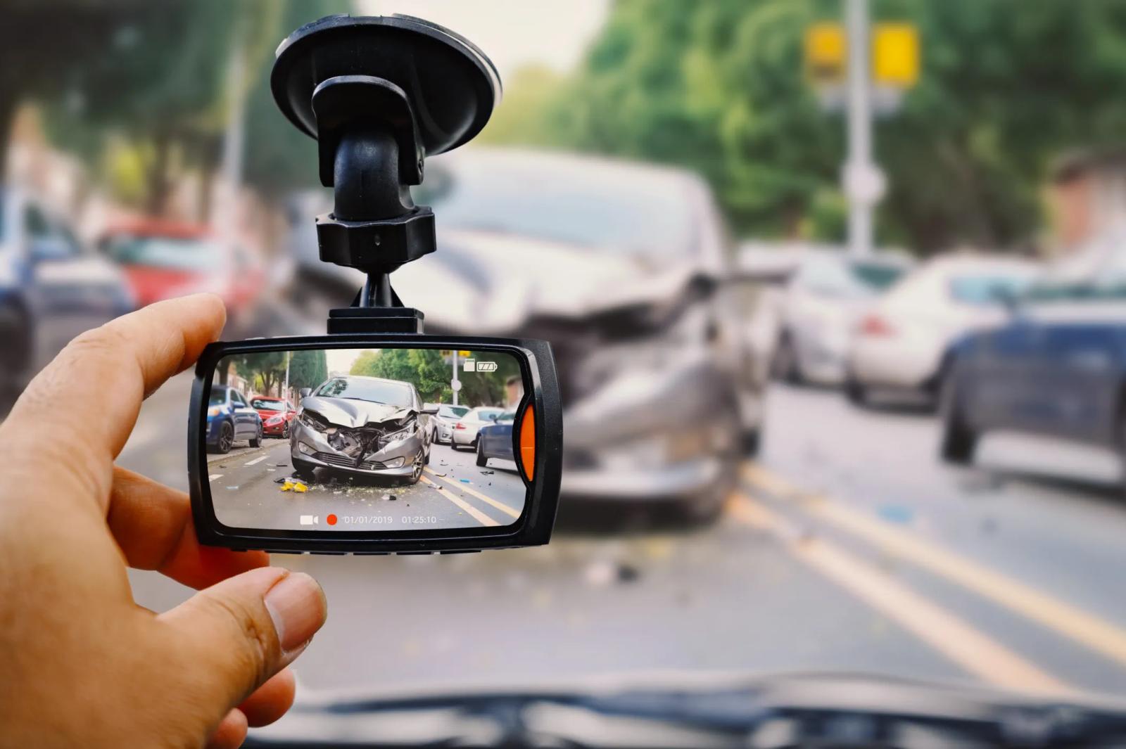 A dash camera held up in front of a wrecked car at a roadside collision