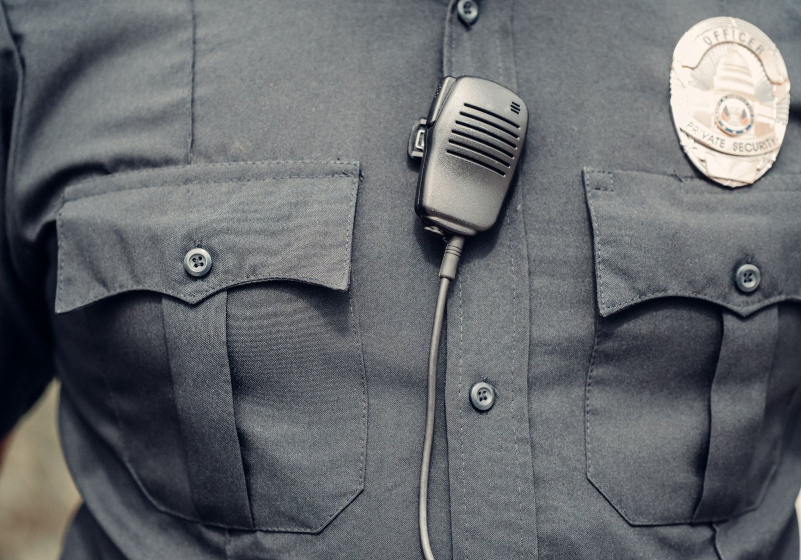 Close-up of a uniform shirt with a shoulder radio and a Private Security badge
