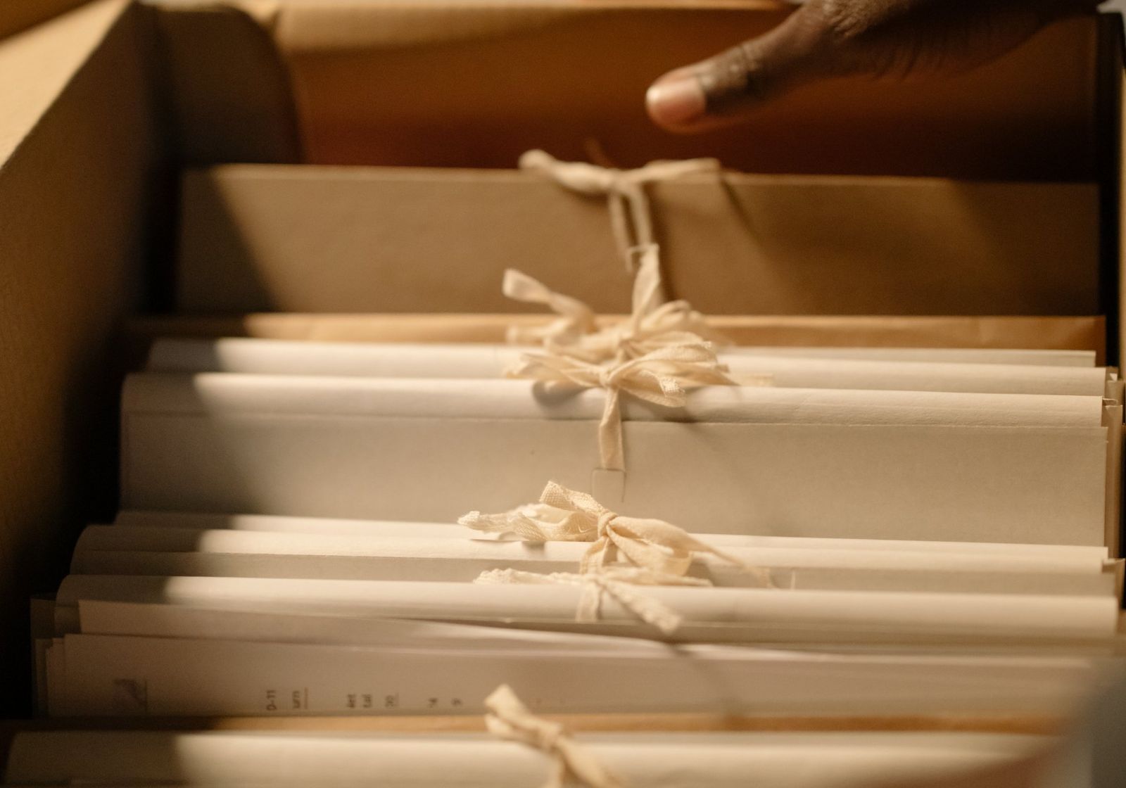 A hand lifting a bundle of tied paper files out of a records box