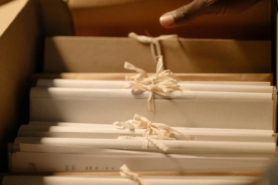 A hand lifting a bundle of tied paper files out of a records box