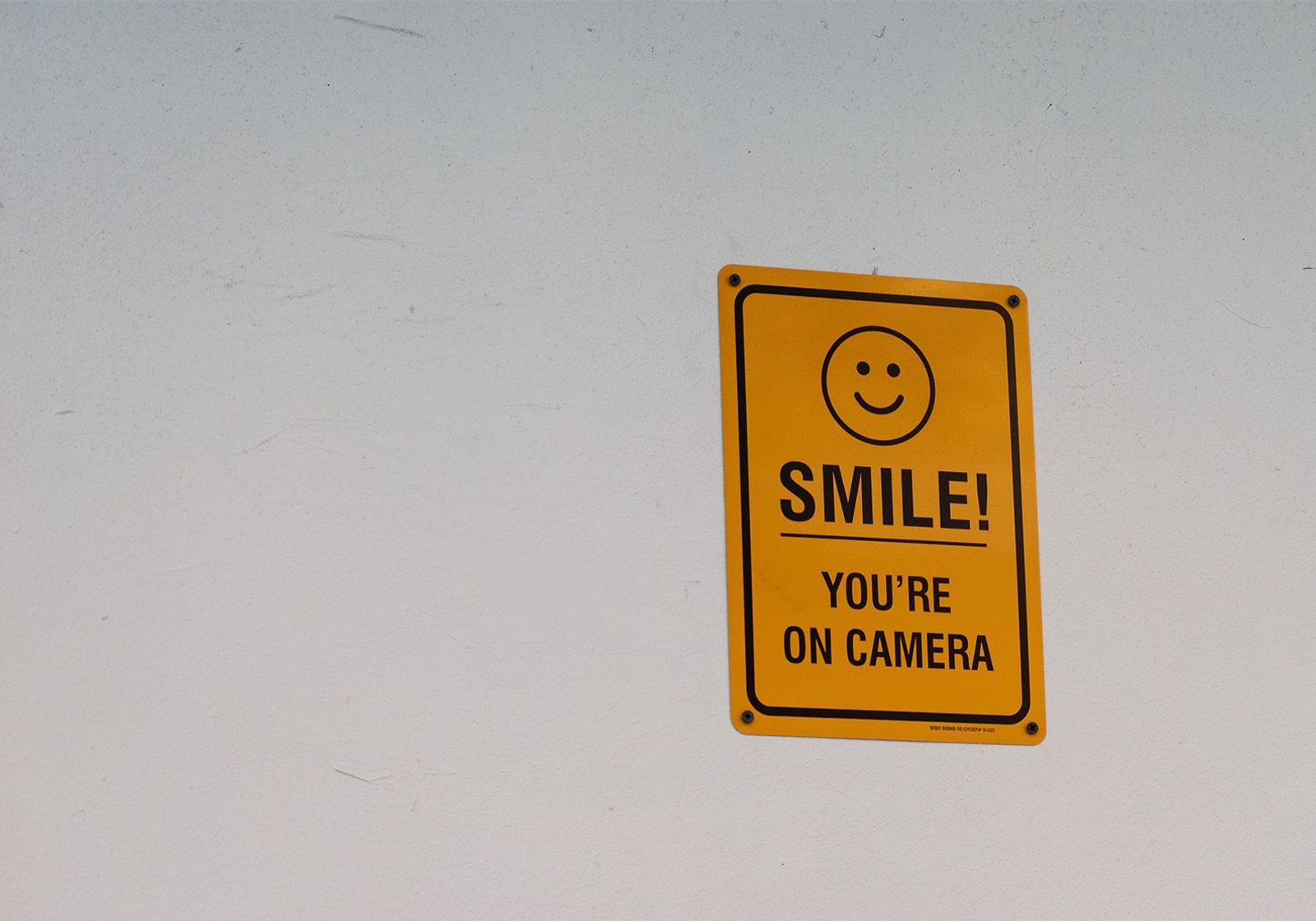 A yellow sign on a wall that says "Smile! You're on camera"