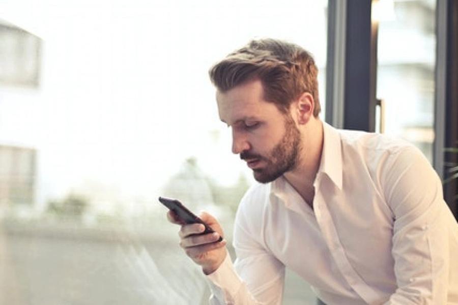 A man standing at a window, studying the screen of his phone