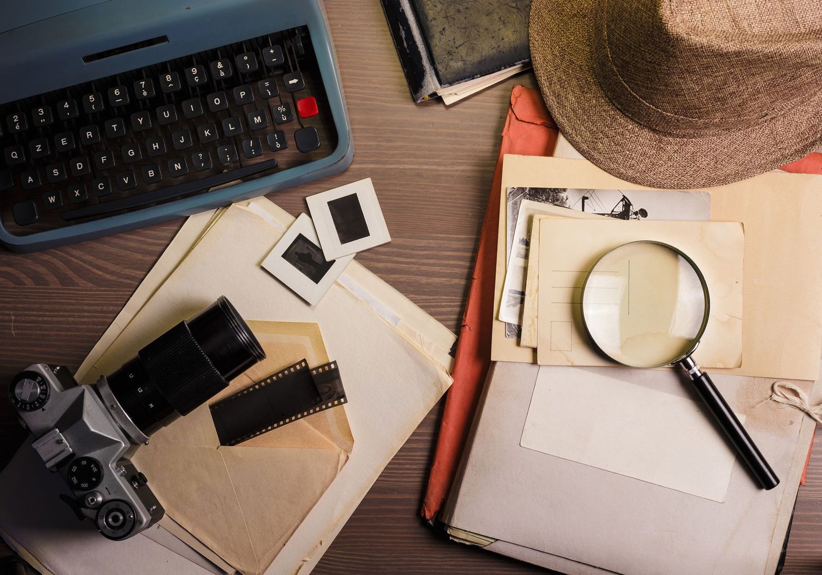 A flat lay of vintage detective gear: a typewriter, a film camera, a magnifying glass and a fedora