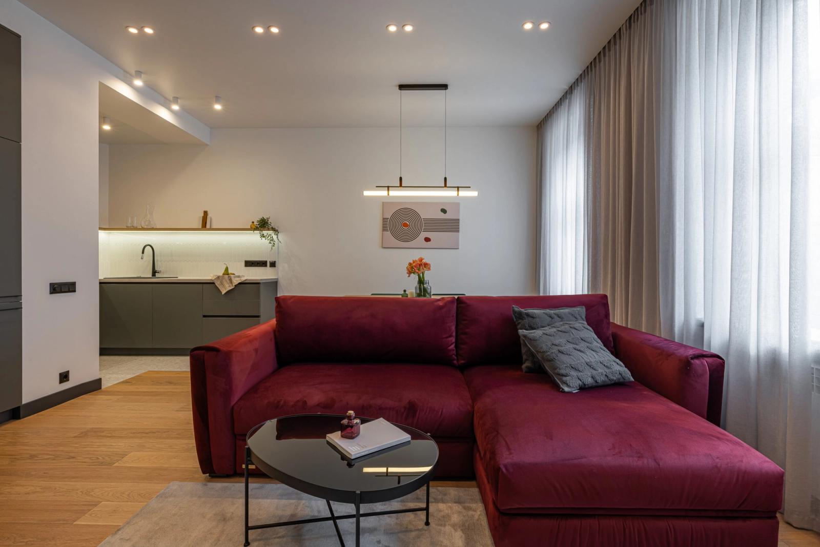 Living room with plush burgundy sectional and modern pendant light, Reitarska 30, Kyiv — Vestor.Estate
