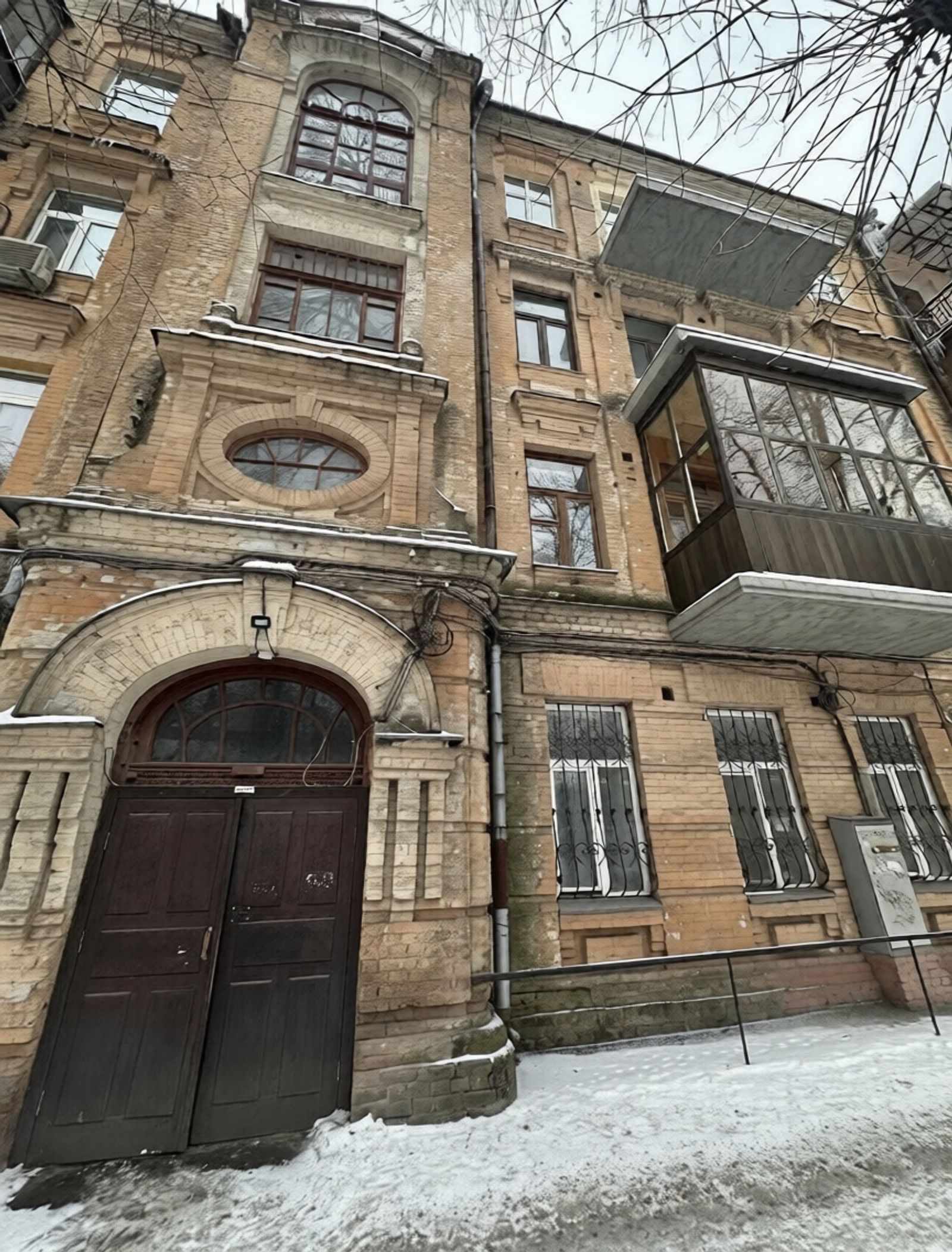 Ornate brick building facade with arched entryway and enclosed balcony, Yaroslaviv Val 21YE, Kyiv — Vestor.Estate