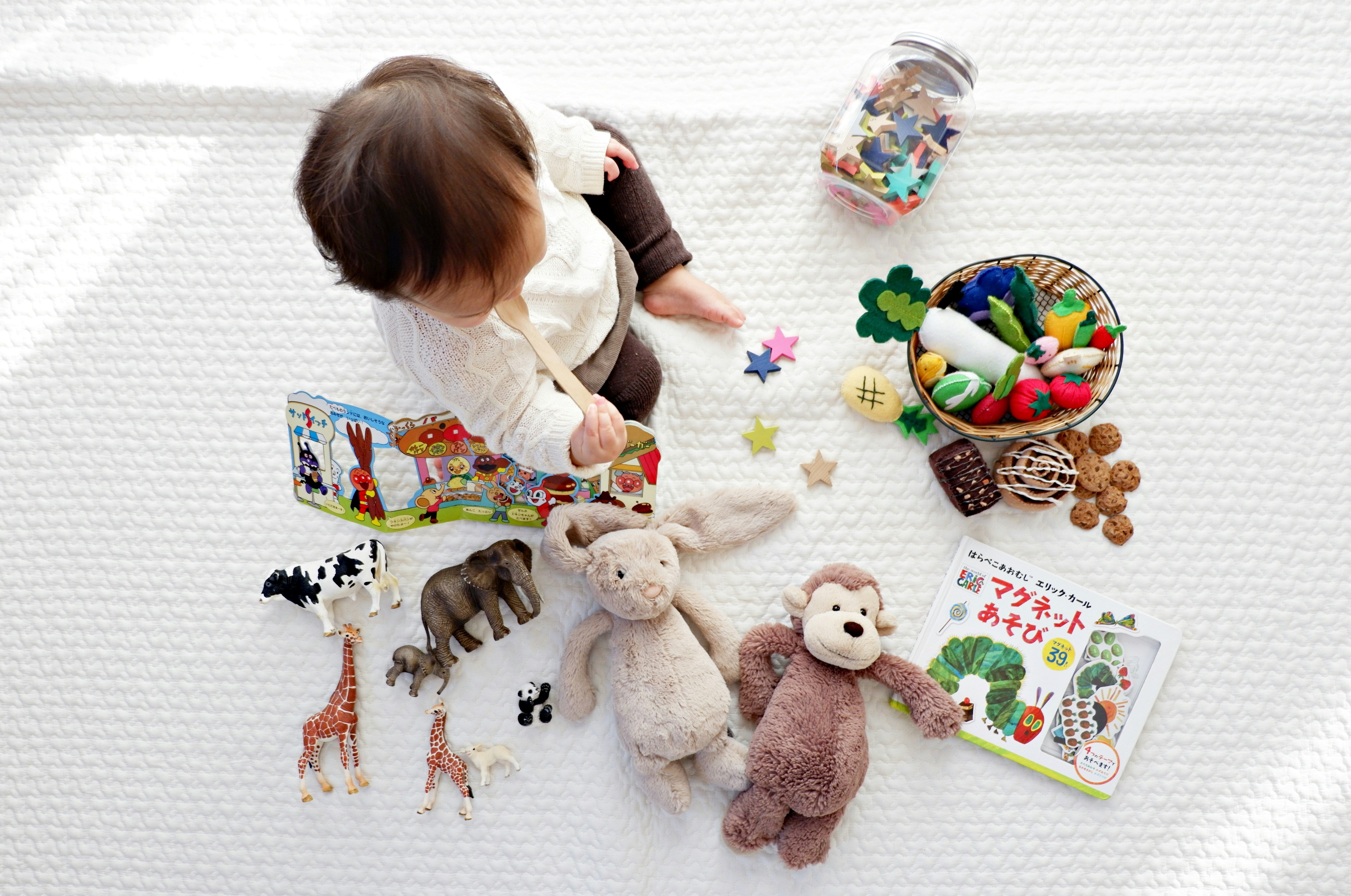 A young child sitting surrounded by colourful toys in a bright, open space
