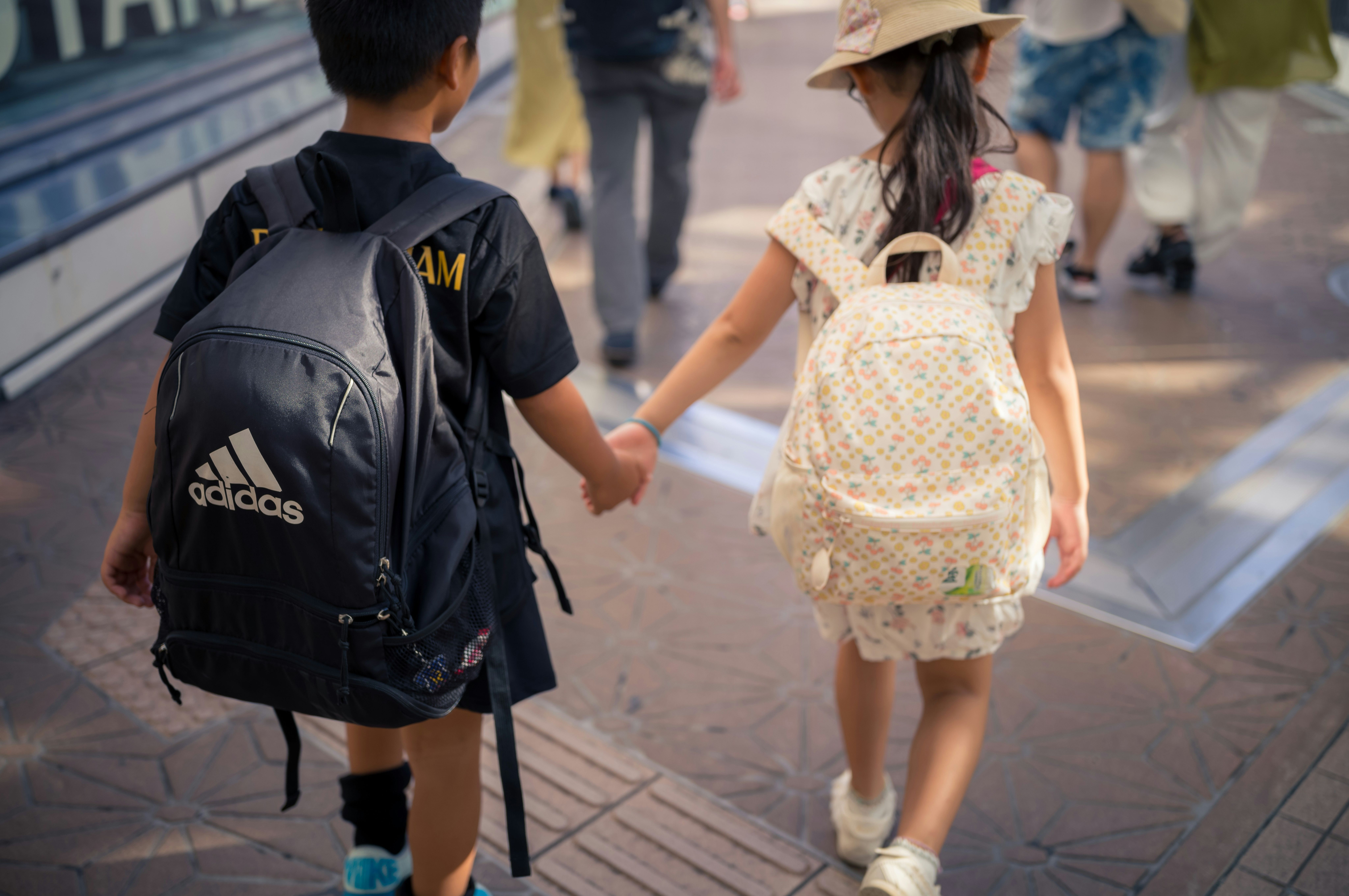 Two children holding hands walking down a street together