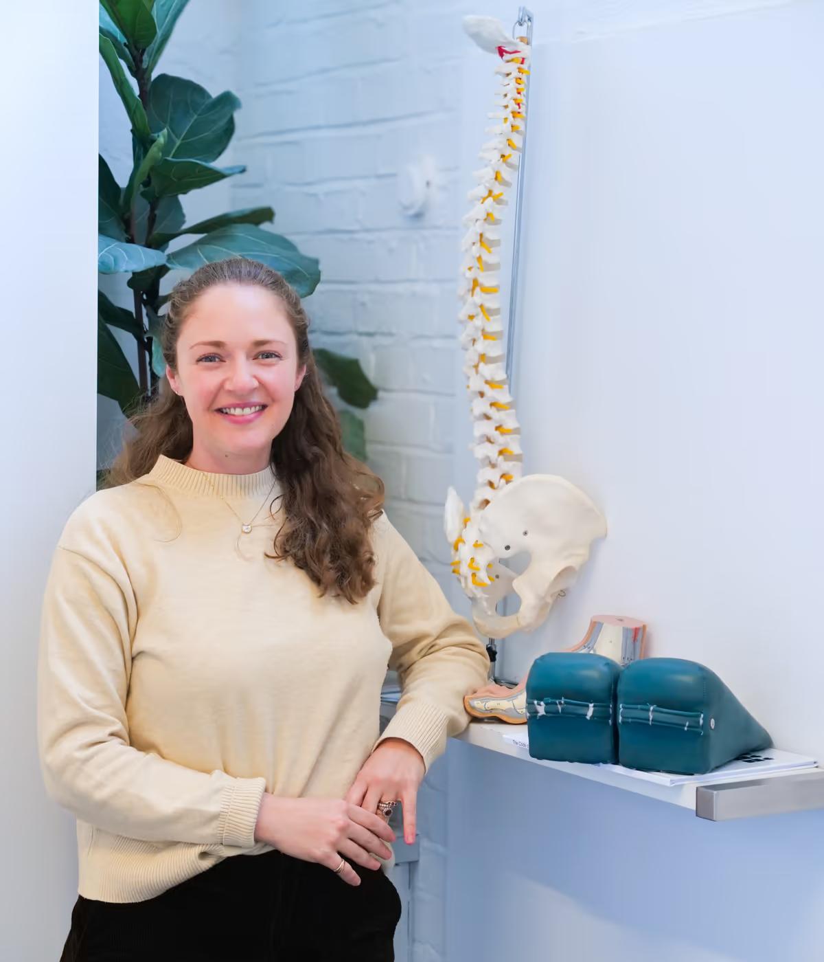 A Chiro London chiropractor smiling beside an anatomical spine model in the clinic