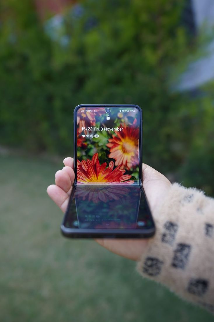 Close-up of a hand holding a foldable smartphone showing a floral wallpaper outdoors.