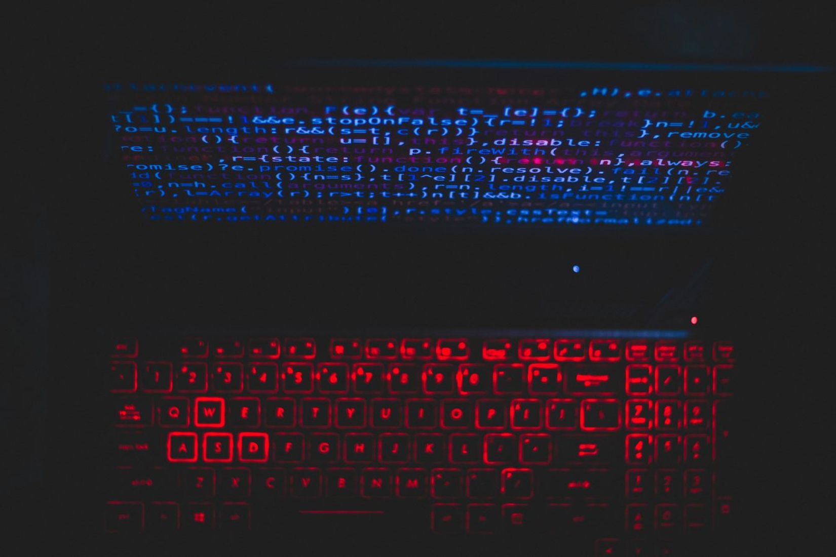 Dark-themed laptop setup with code on screen and red backlit keyboard.