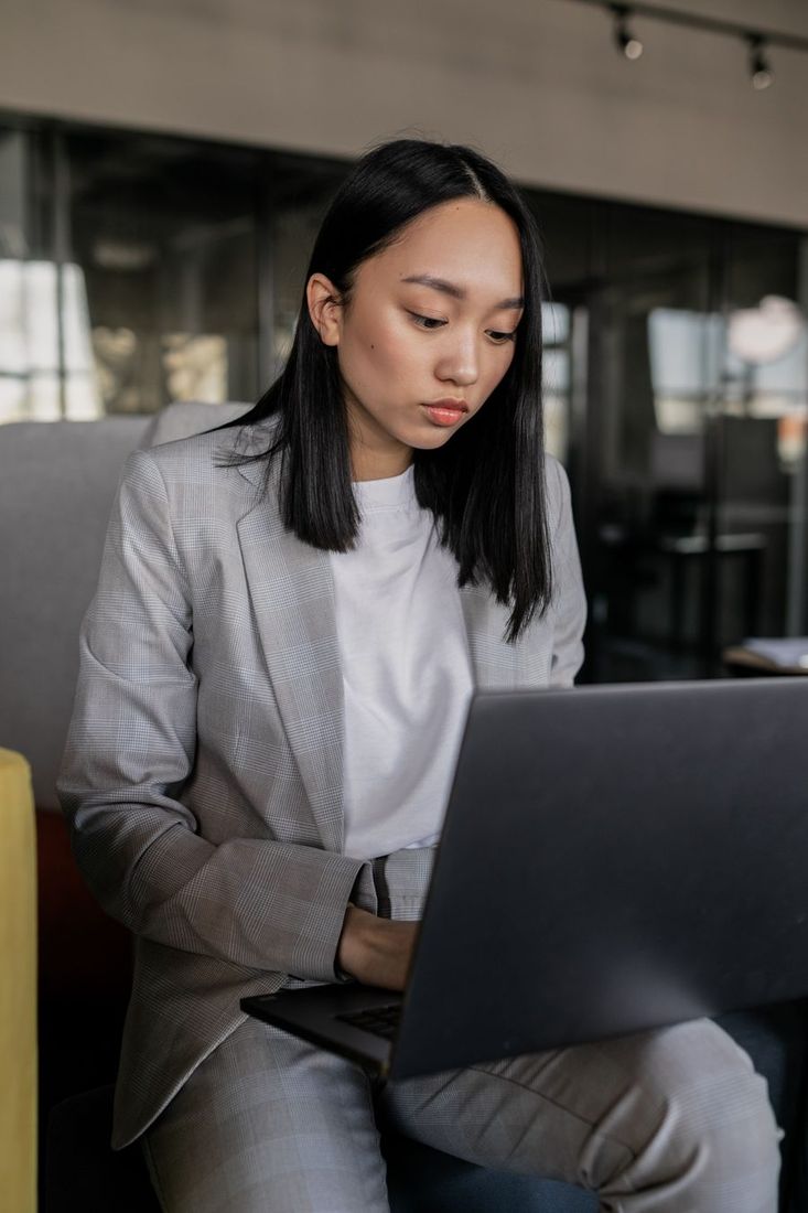 Focused Asian woman in business attire working on laptop in a modern office setting
