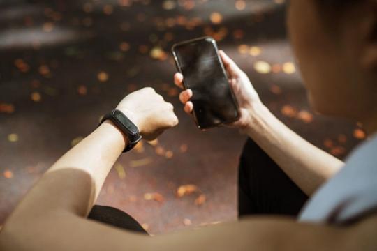 Bėgikė parke naudojasi telefonu ir išmaniuoju laikrodžiu. Asociatyvi nuotrauka.
