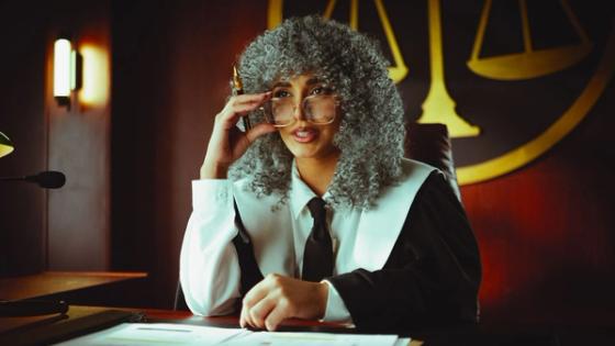 An elegant judge in robes sits at a desk in a courtroom, poised and authoritative.