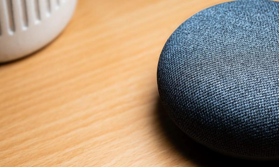 A close-up view of a smart speaker on a wooden table, capturing texture details.
